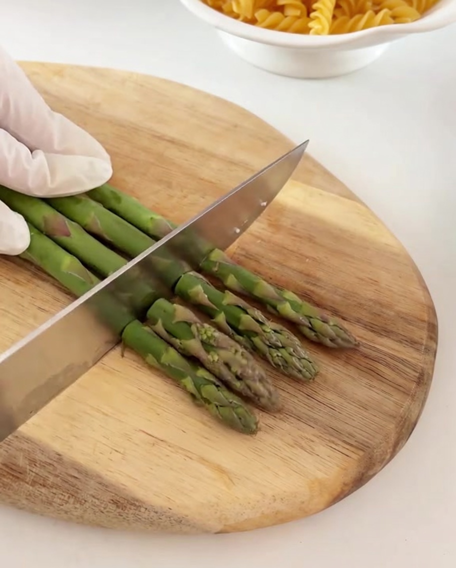 Fresh green asparagus stalks being chopped into smaller pieces on a wooden board.