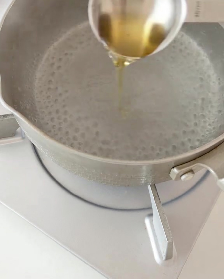 Dry fusilli pasta being added to a pot of boiling water with a splash of oil.