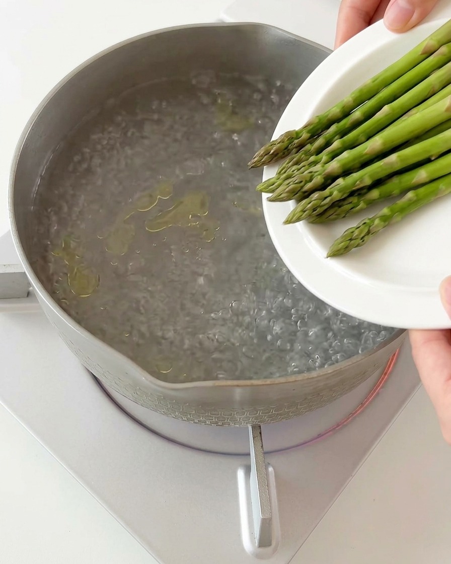Sliced asparagus pieces being dropped into a pot of boiling water.