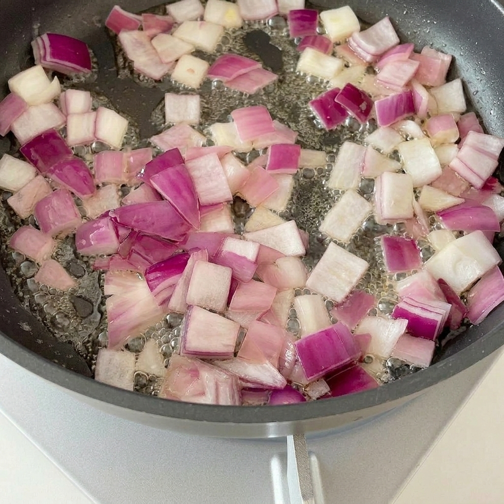 Bacon pieces frying in a pan with sautéed onions.