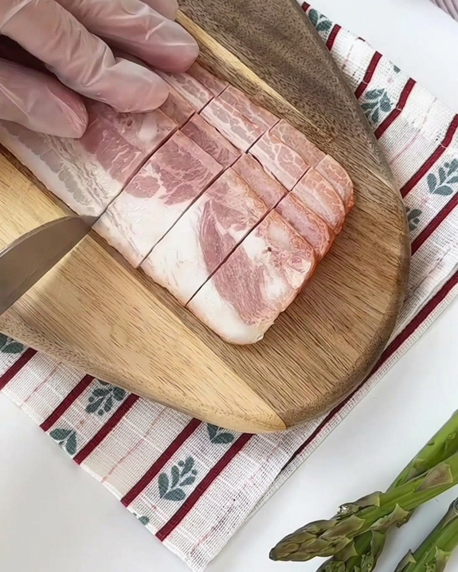 Fresh green asparagus stalks being cut into equal-sized segments on a wooden cutting board.