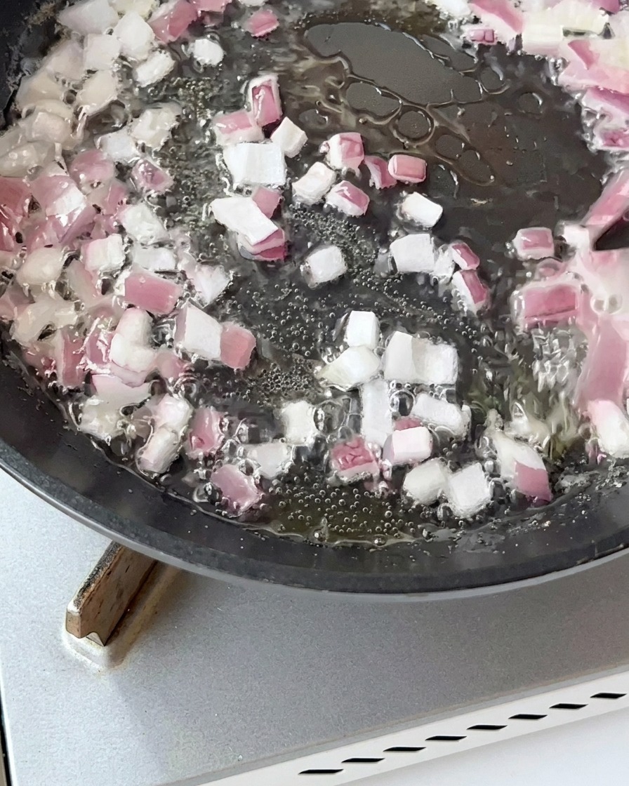 Bacon pieces stir-frying in a pan with sautéed onions until golden brown.
