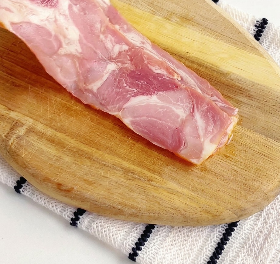 Raw bacon strips being cut into smaller pieces on a wooden cutting board.