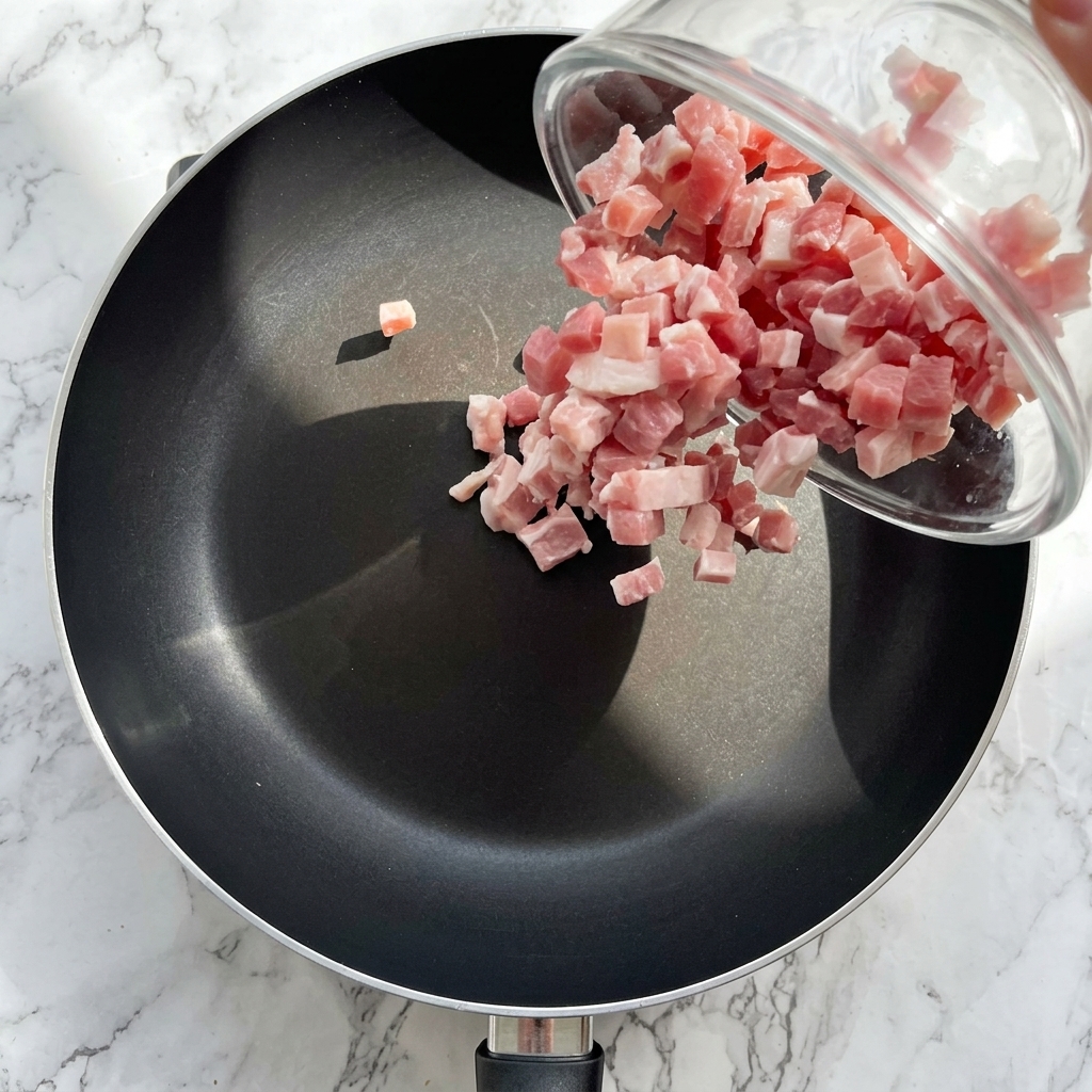 Diced bacon frying in a skillet until browned and crispy.