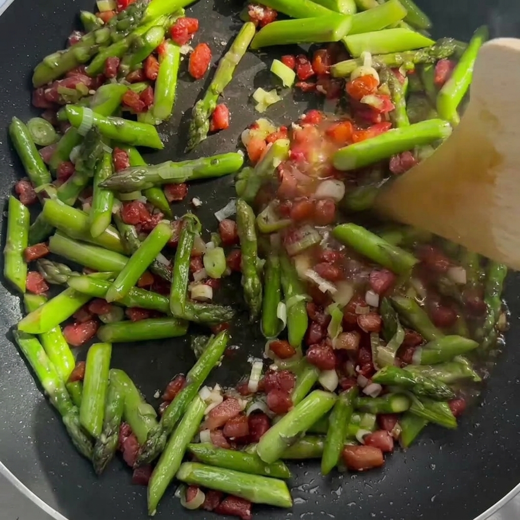 Cream being stirred into the sautéed bacon and asparagus in the pan.