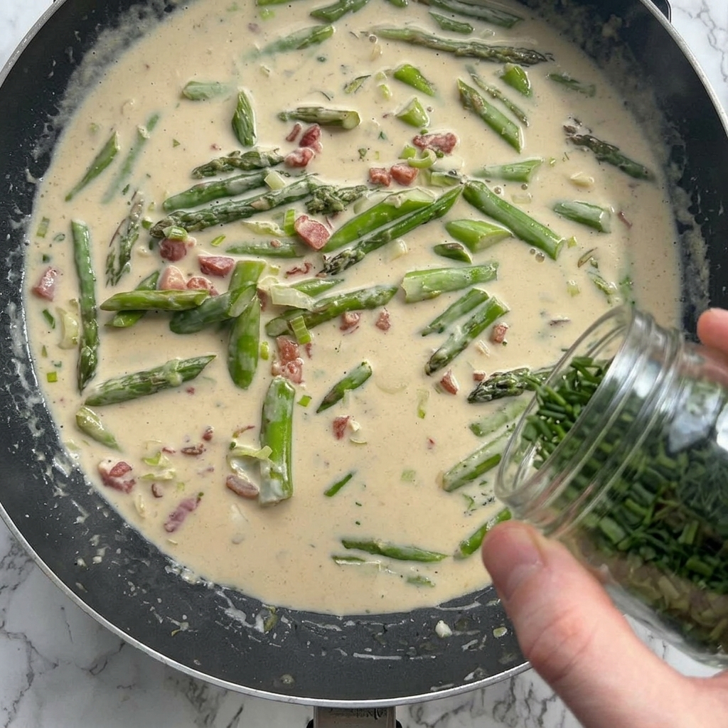 Parmesan cheese and herbs being added to the creamy sauce in the skillet.