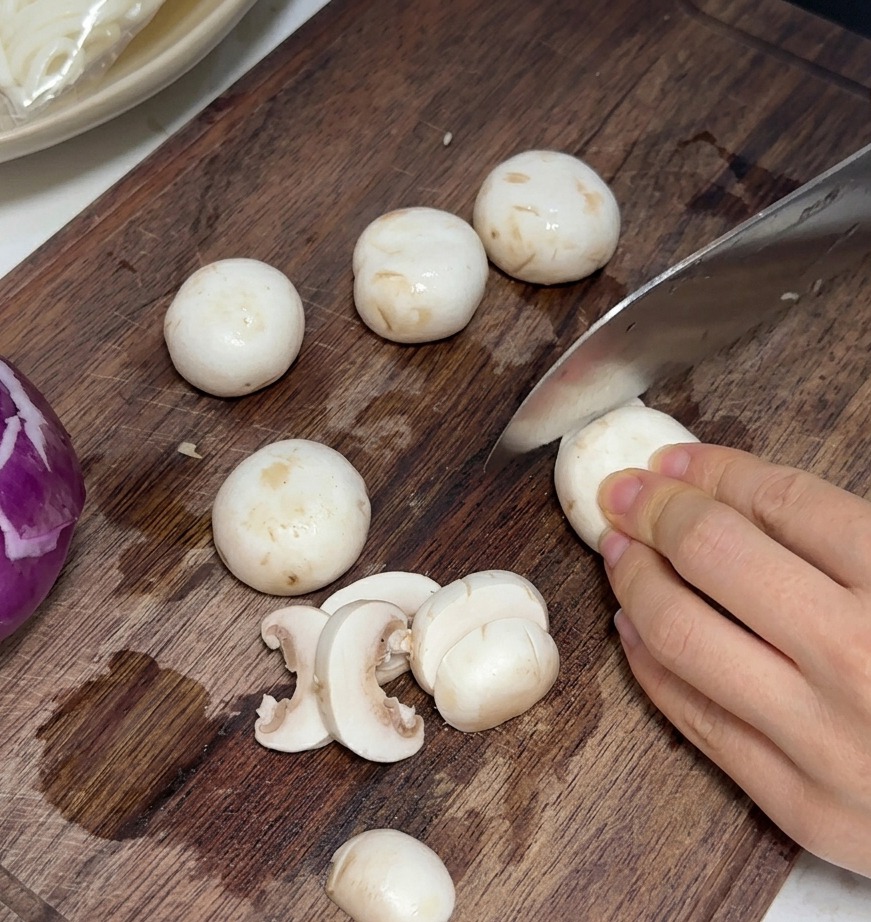 Fresh mushrooms being sliced into thin, even pieces on a wooden cutting board.