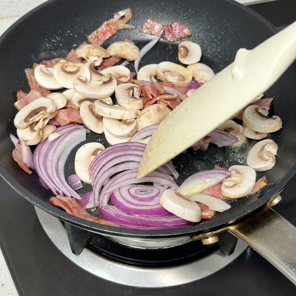 Sliced red onions and mushrooms stir-frying in a pan with bacon and butter.