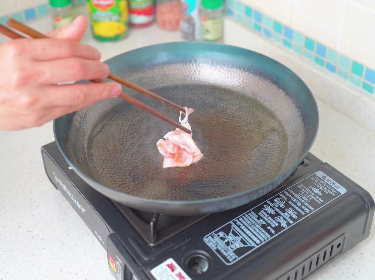 Crispy golden-brown bacon pieces frying in a pan.