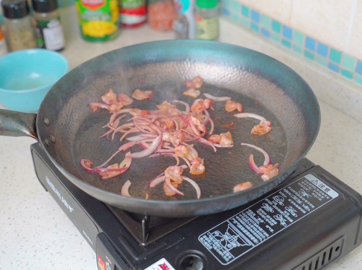 Onion slices and mushrooms cooking in a pan with fried bacon pieces.