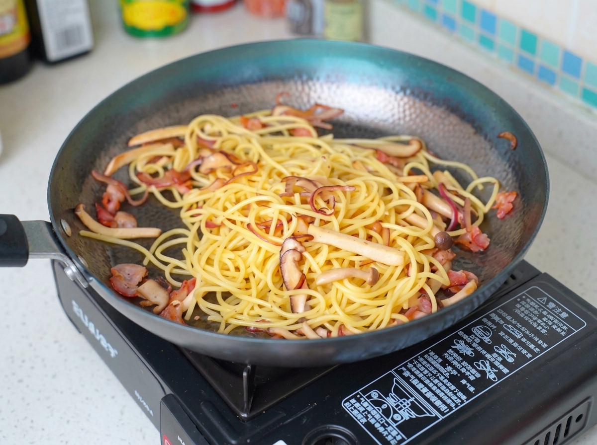 Milk being poured over the pasta, bacon, and mushroom mixture in a pan.