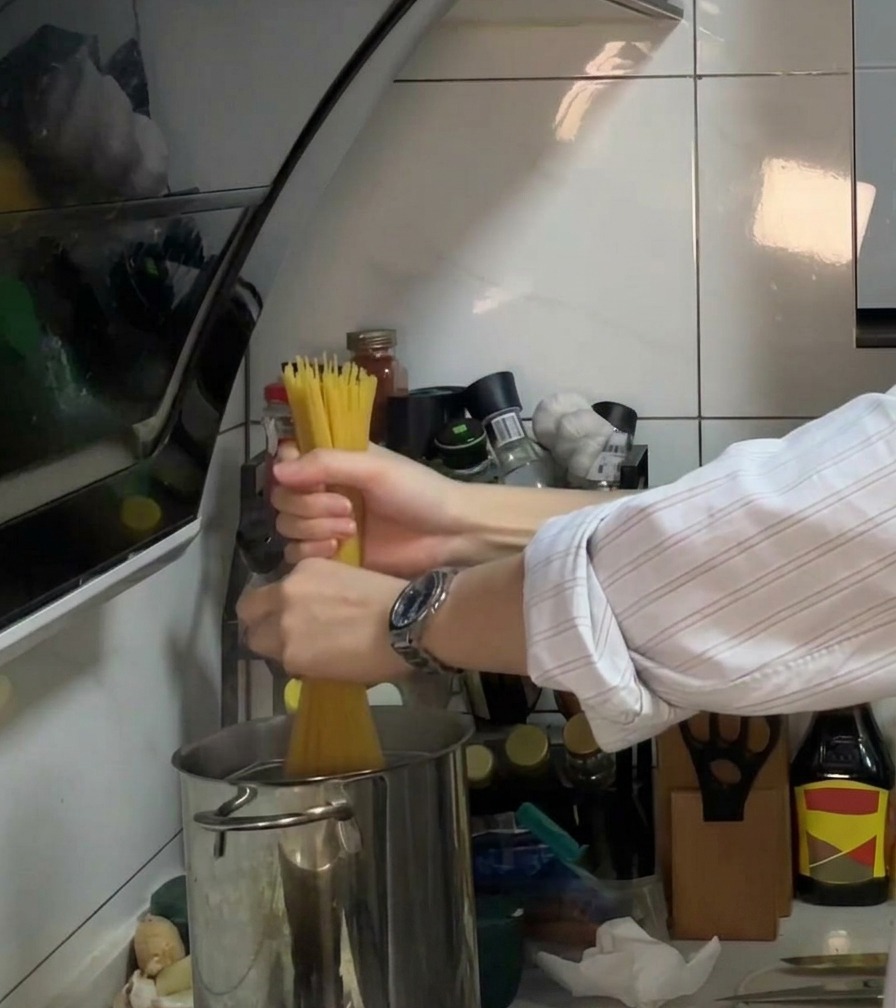 Spaghetti being placed into a pot of bubbling boiling water with oil and salt.
