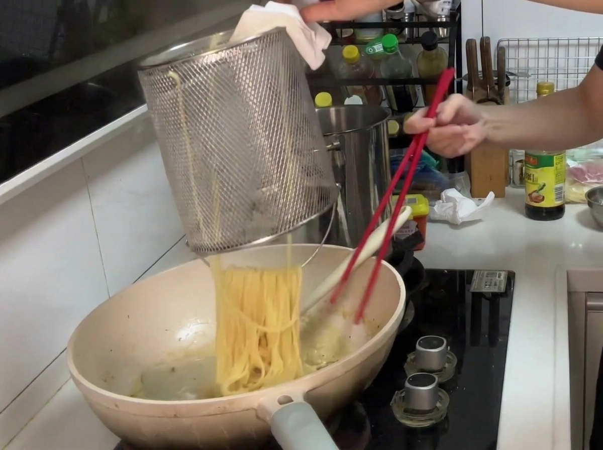 Pasta being transferred from a strainer into a pan of creamy mushroom sauce, ready for tossing.