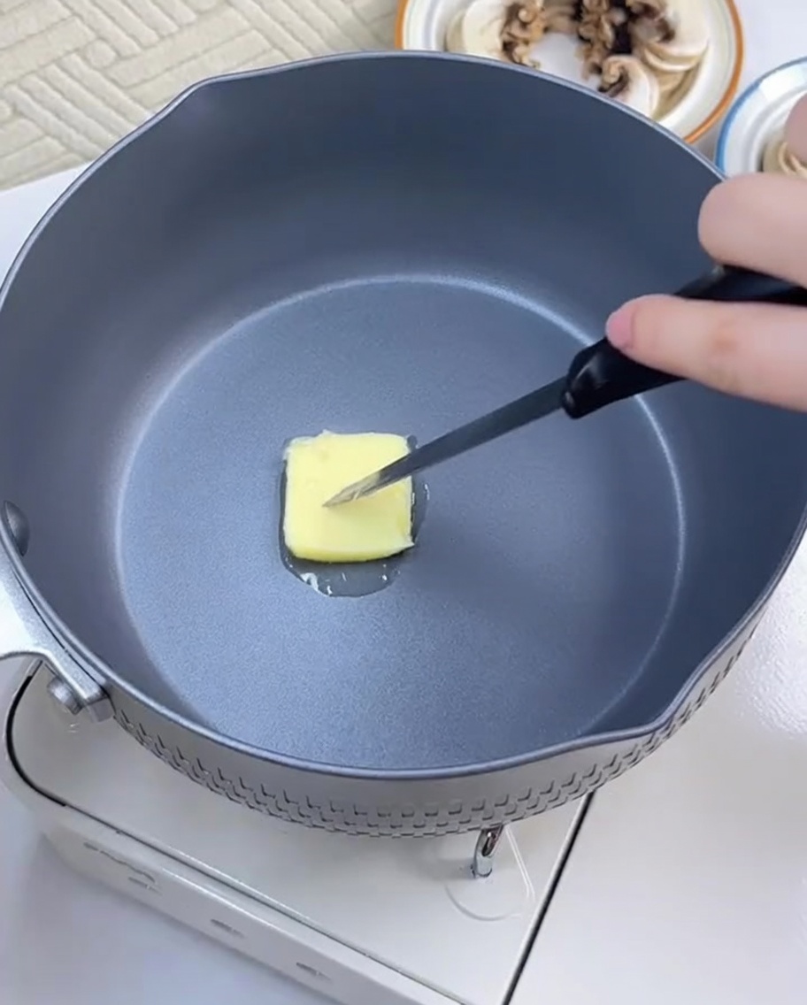 Close up of garlic slices sizzling in melting butter in a pan.