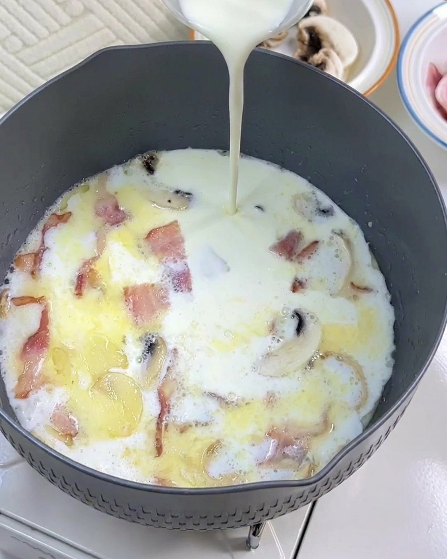 Heavy cream being added to the pan with the milk, bacon, and mushrooms.