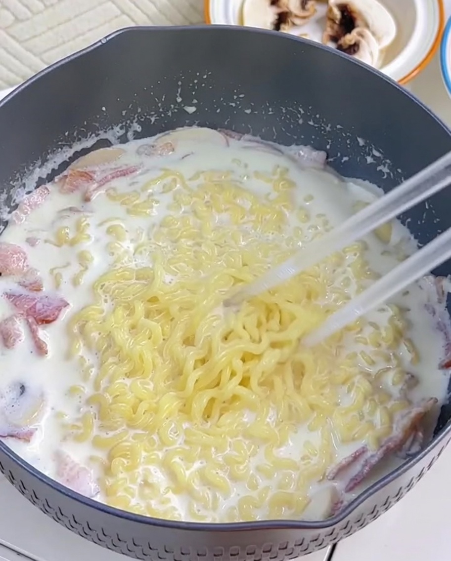 Ramen noodles being incorporated into the creamy sauce using chopsticks.