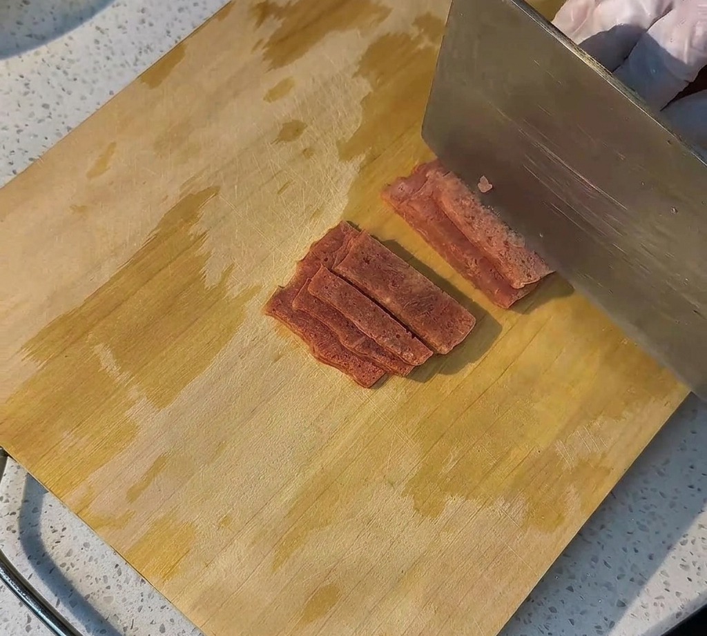 Slices of raw bacon neatly arranged on a wooden board ready for cooking.