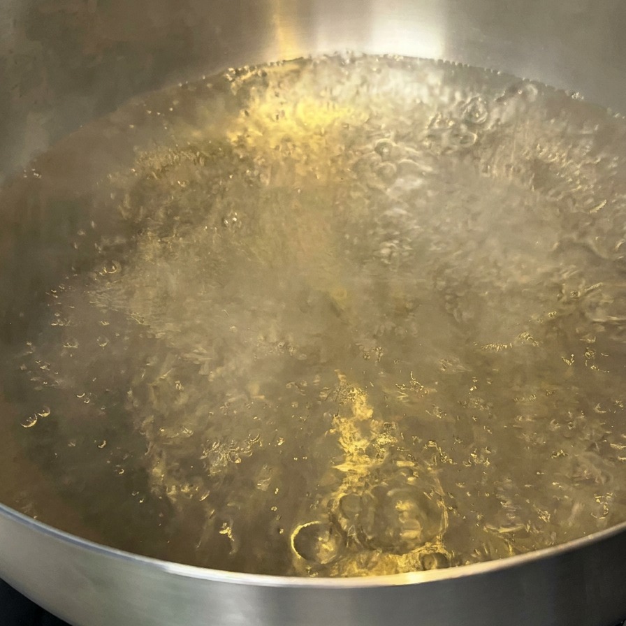 A pot of boiling water with a small amount of oil floating on the surface.