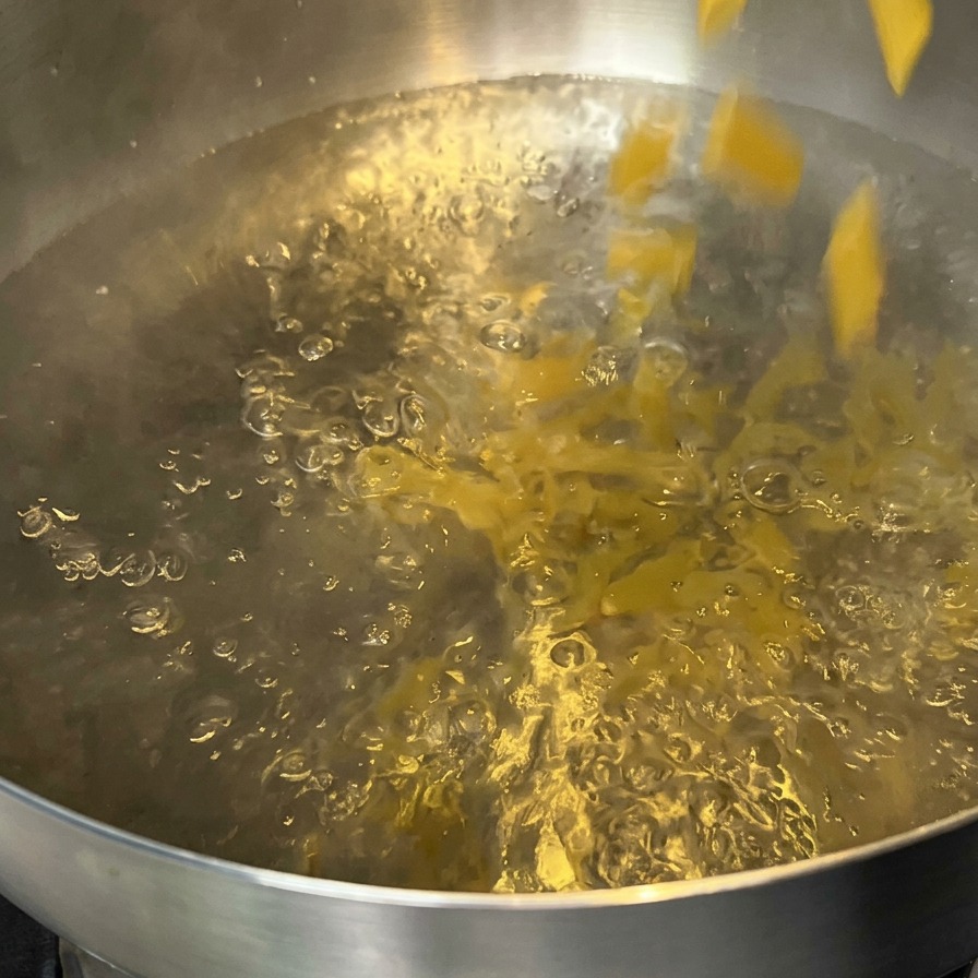 Penne pasta being poured into a pot of boiling water.