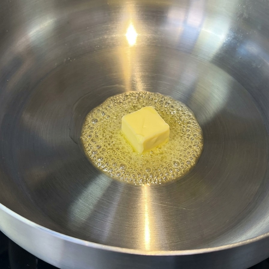 Butter melting in a stainless steel pan, showing golden liquid bubbles.