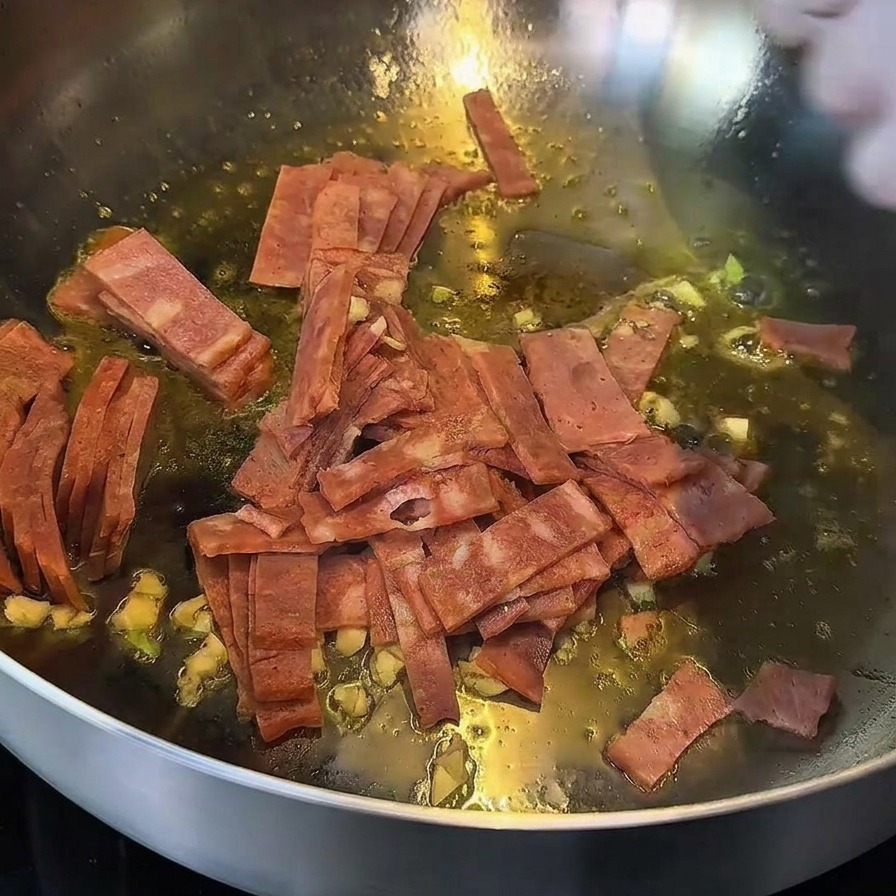 Bacon and garlic sautéing in a pan, with bacon edges looking golden brown.