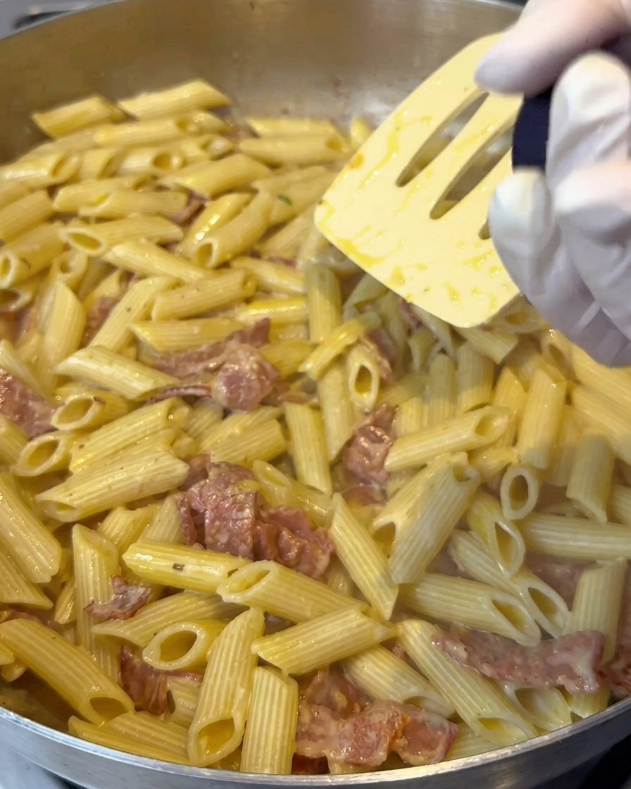 Lemon salt being ground over a pan of creamy penne pasta as it is stirred.