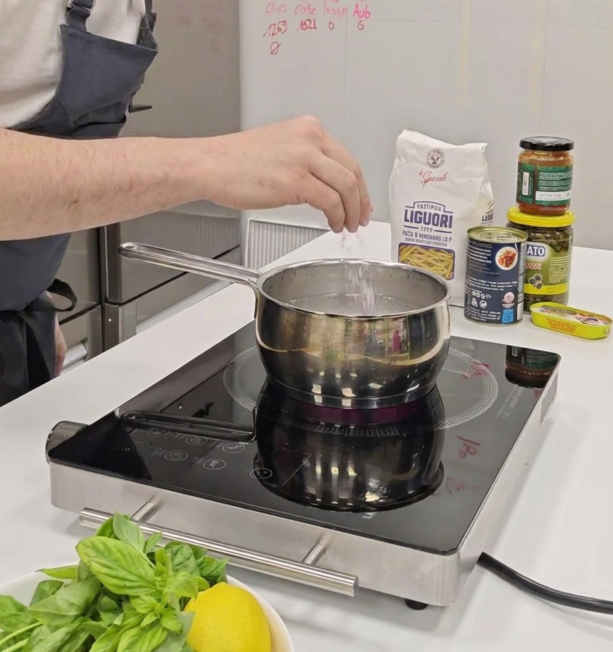 A persons hand sprinkling a pinch of salt into a pot of water on an induction stove.