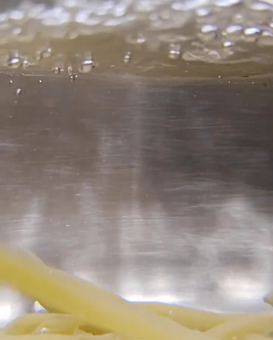 Close-up of dry twisted Trofie pasta submerged in vigorously bubbling water.