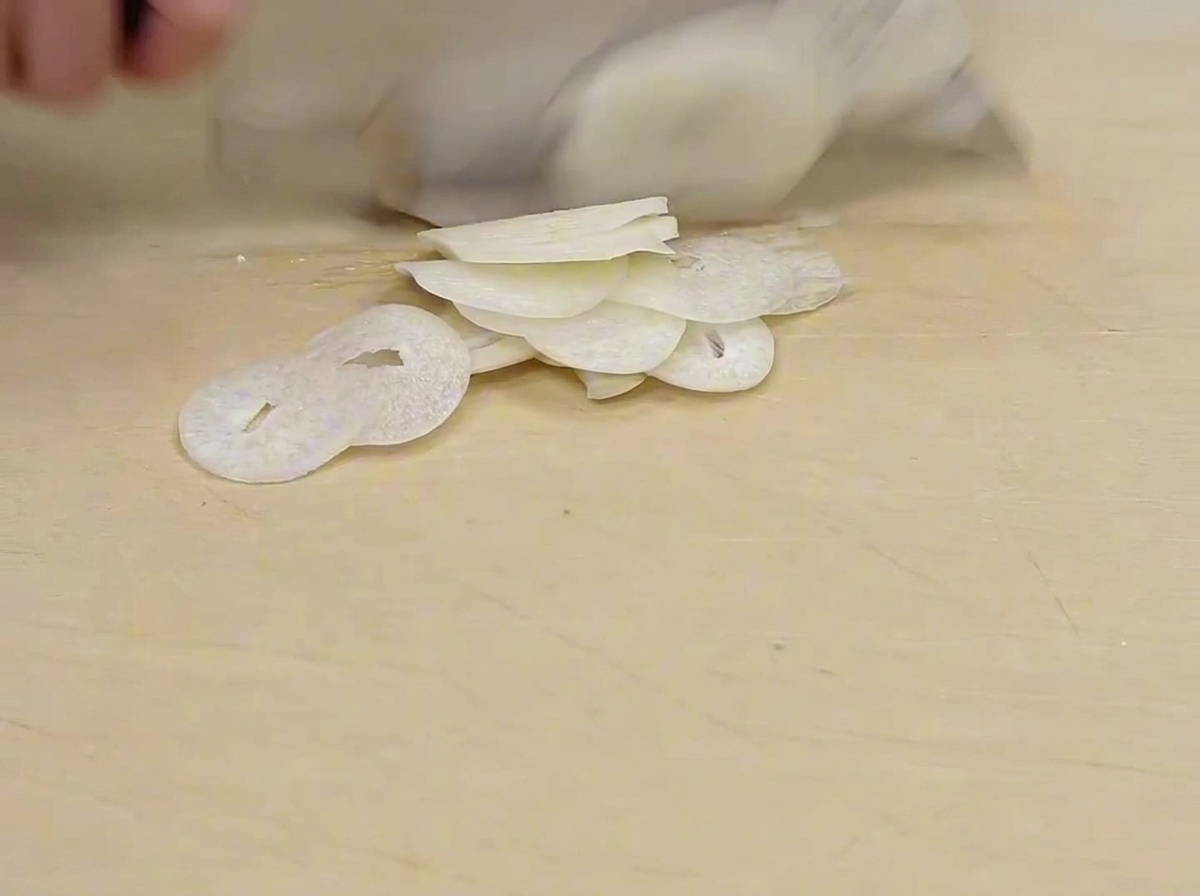 Extremely thin, nearly translucent slices of garlic on a light-colored wooden cutting board.
