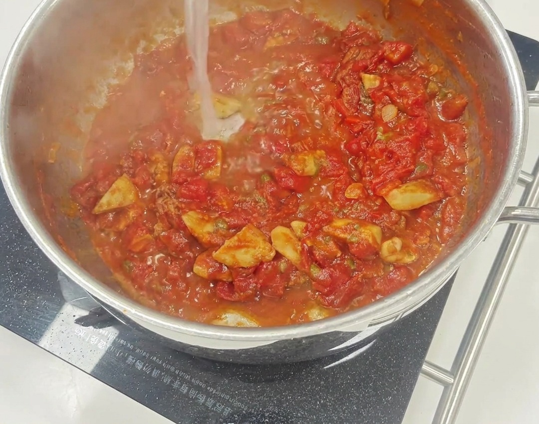 A vibrant red tomato sauce simmering in a skillet with visible pieces of sun-dried tomatoes and capers.