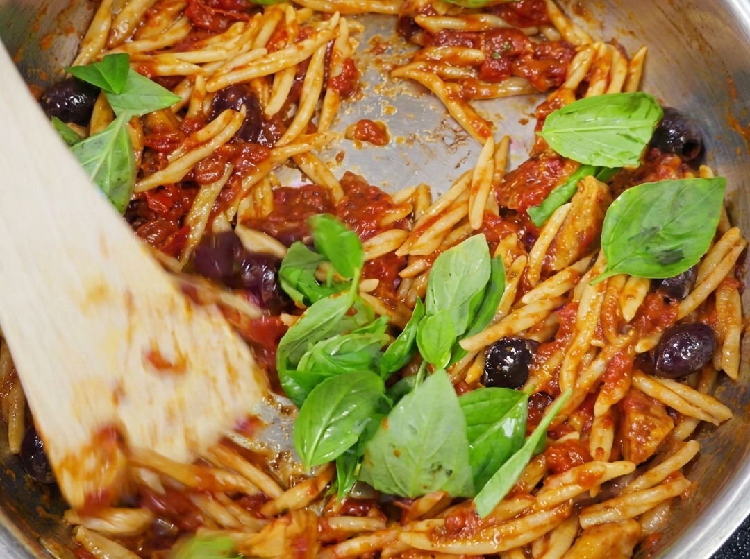 Finished Trofie pasta tossed in Puttanesca sauce and garnished with fresh green basil leaves.