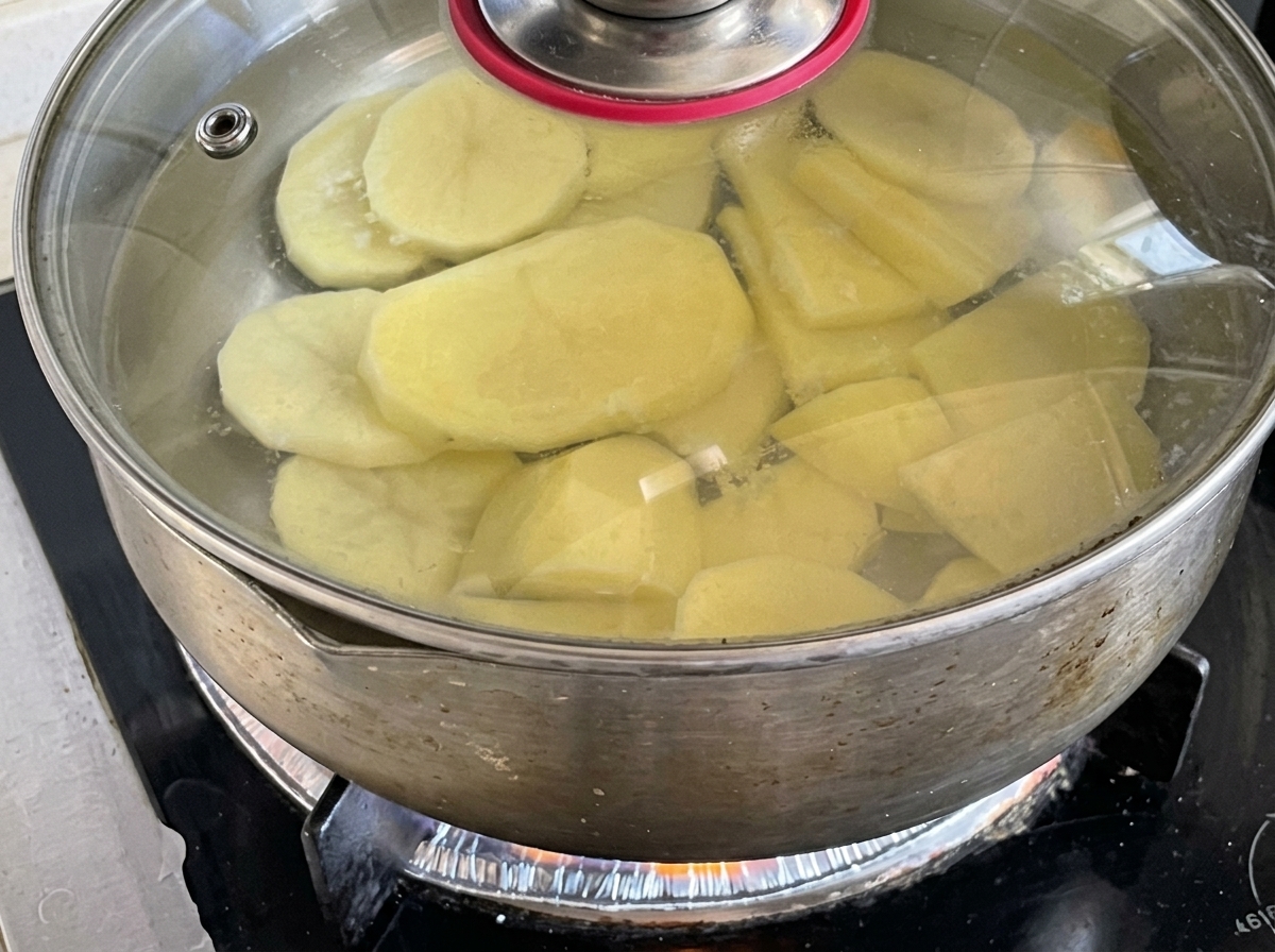 Potato slices simmering in a covered pot of water on the stove.