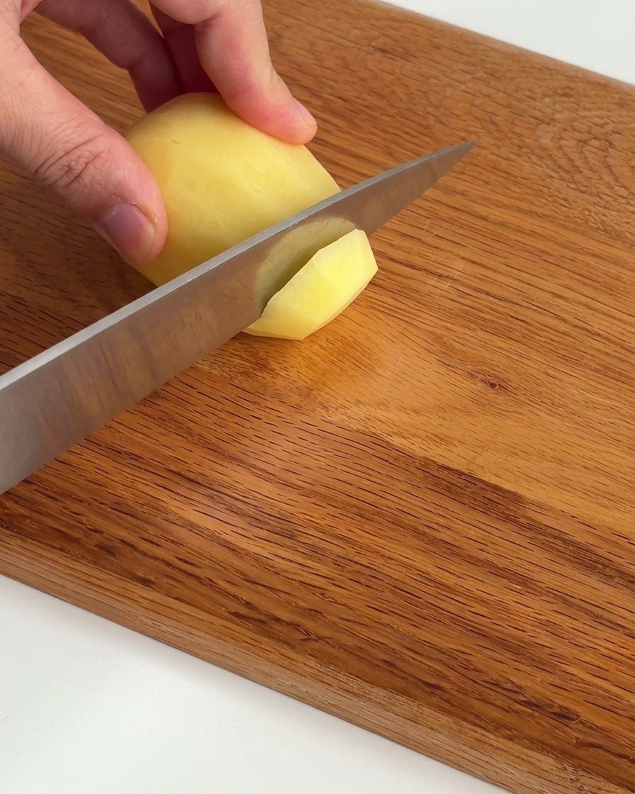 Thinly sliced raw potatoes neatly arranged on a wooden cutting board.