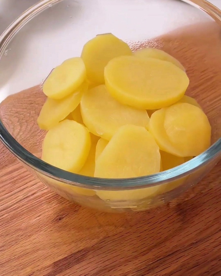 Steamed potato slices in a bowl with visible black pepper and white starch powder on top.
