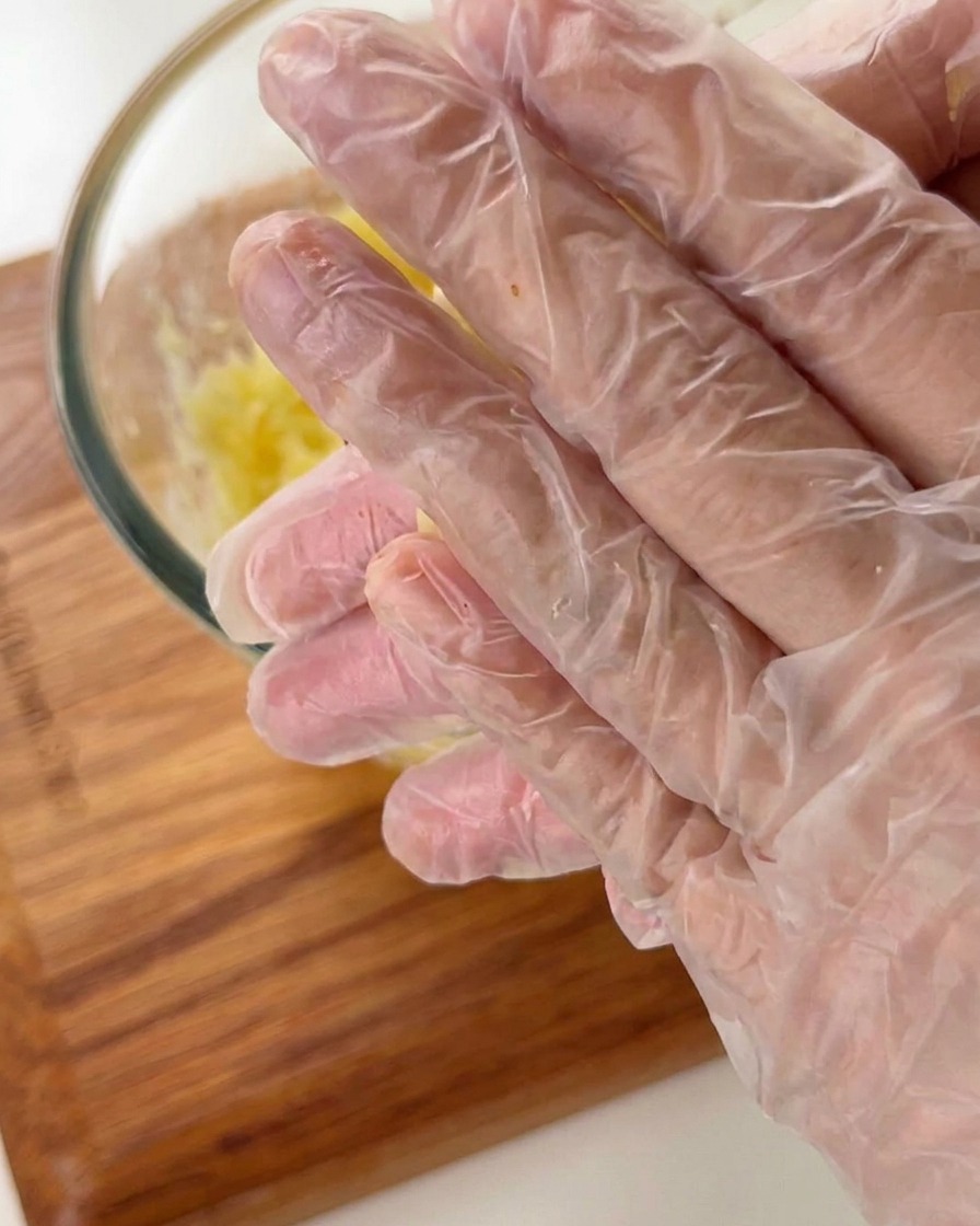 Hands wearing plastic gloves shaping potato paste into a small bowl-like tart shell.