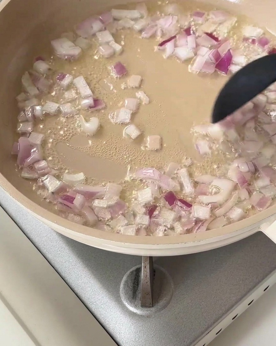 Red onion cubes sizzling in a pan with hot cooking oil.