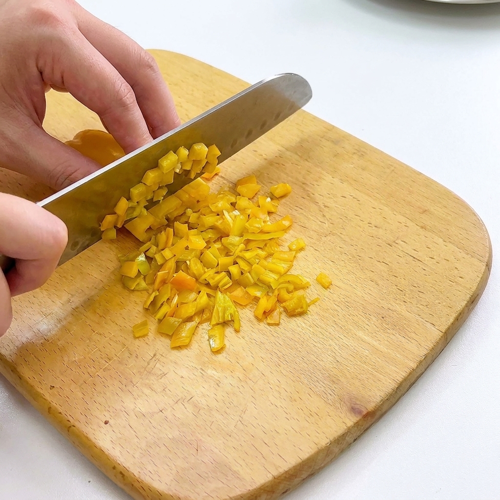 Bell peppers and onions being finely diced on a wooden chopping board.