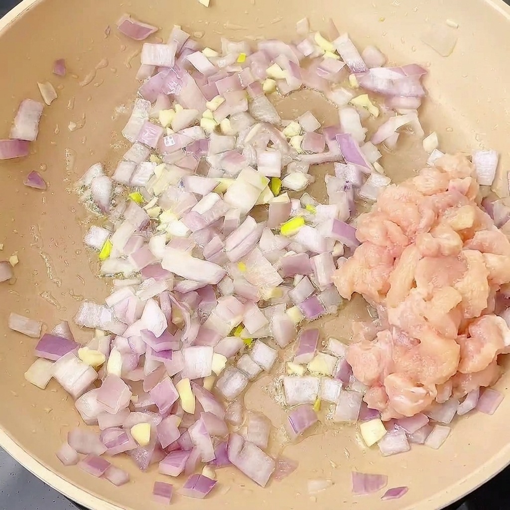 Diced chicken being added to the pan containing sautéed onions and garlic.