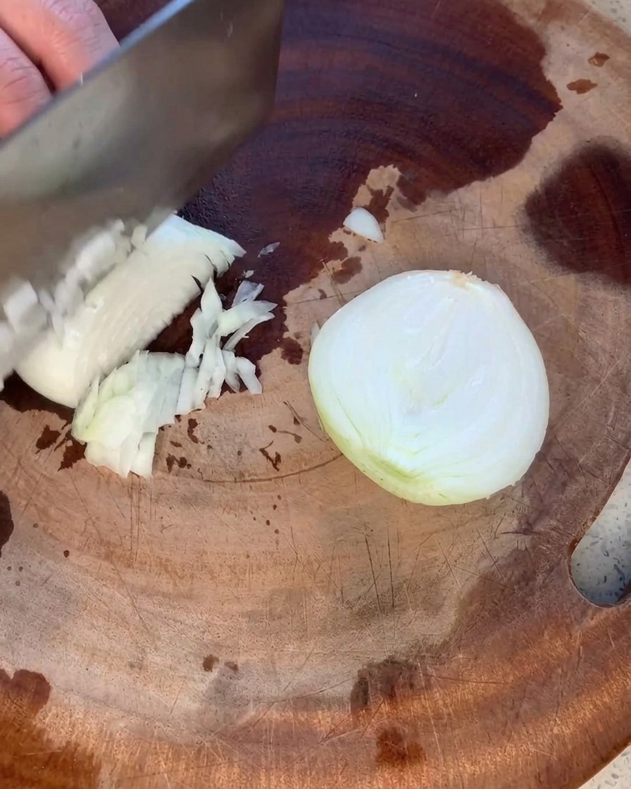 A yellow onion being carefully minced into small, even pieces on a rustic wooden cutting board.