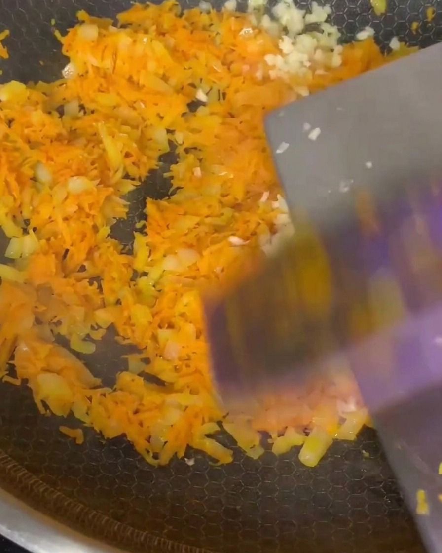 Minced garlic and dried Italian herbs being incorporated into the softened carrot and onion mixture in the pan.