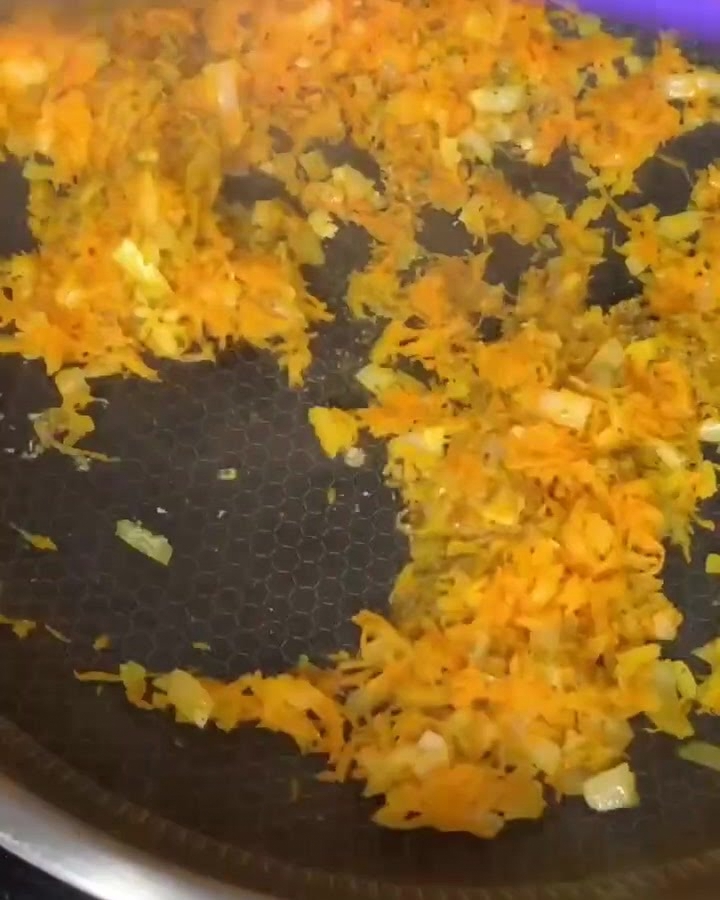 Ground beef being mixed with sautéed carrots and onions in a non-stick frying pan.