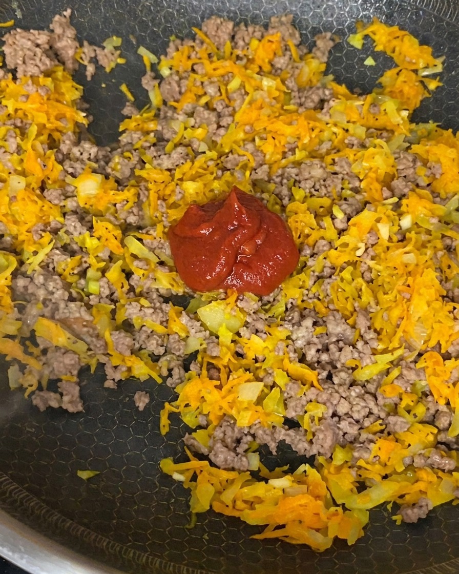 Tomato paste, crushed tomatoes, and soy sauce being stirred into a mixture of browned beef, onions, and carrots.