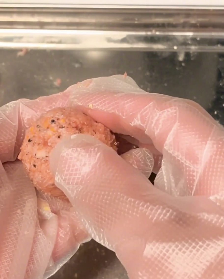 Hands rolling raw ground meat into a round, uniform ball.