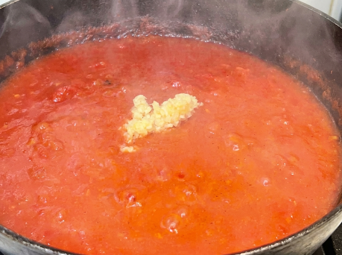 A small mound of minced garlic sitting in the middle of a vibrant, simmering red tomato sauce.