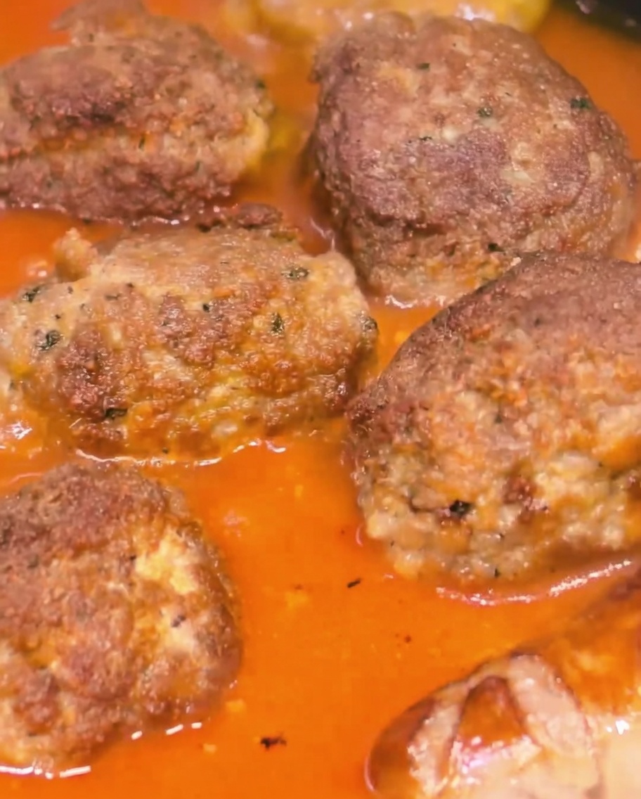 Large meatballs and sausages simmering together in a thick, rich tomato sauce.