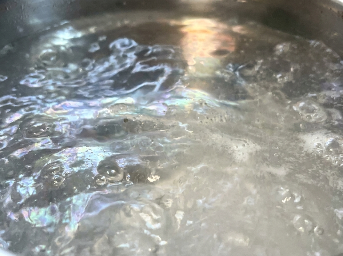 Dry spaghetti pasta strands being submerged into a large pot of violently boiling water.
