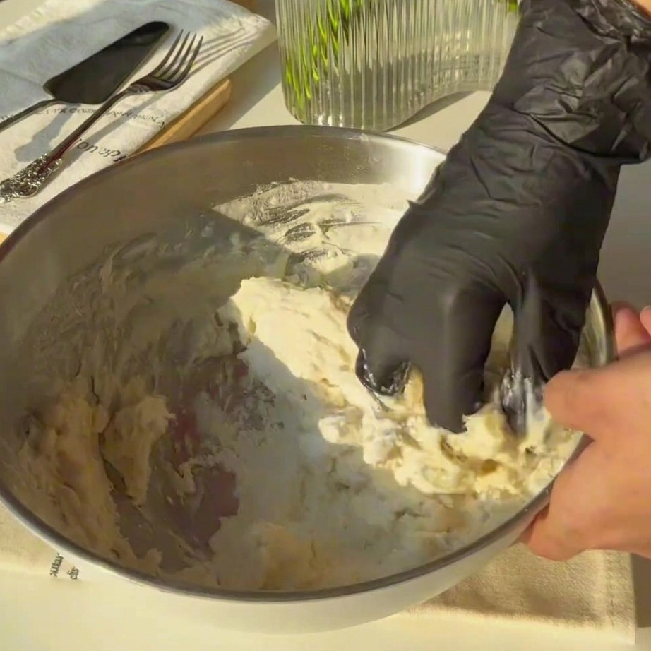 Rough dough being kneaded by hand inside a large metal mixing bowl.