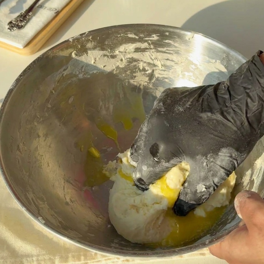 Golden melted butter being poured over a mass of dough in a metal bowl.