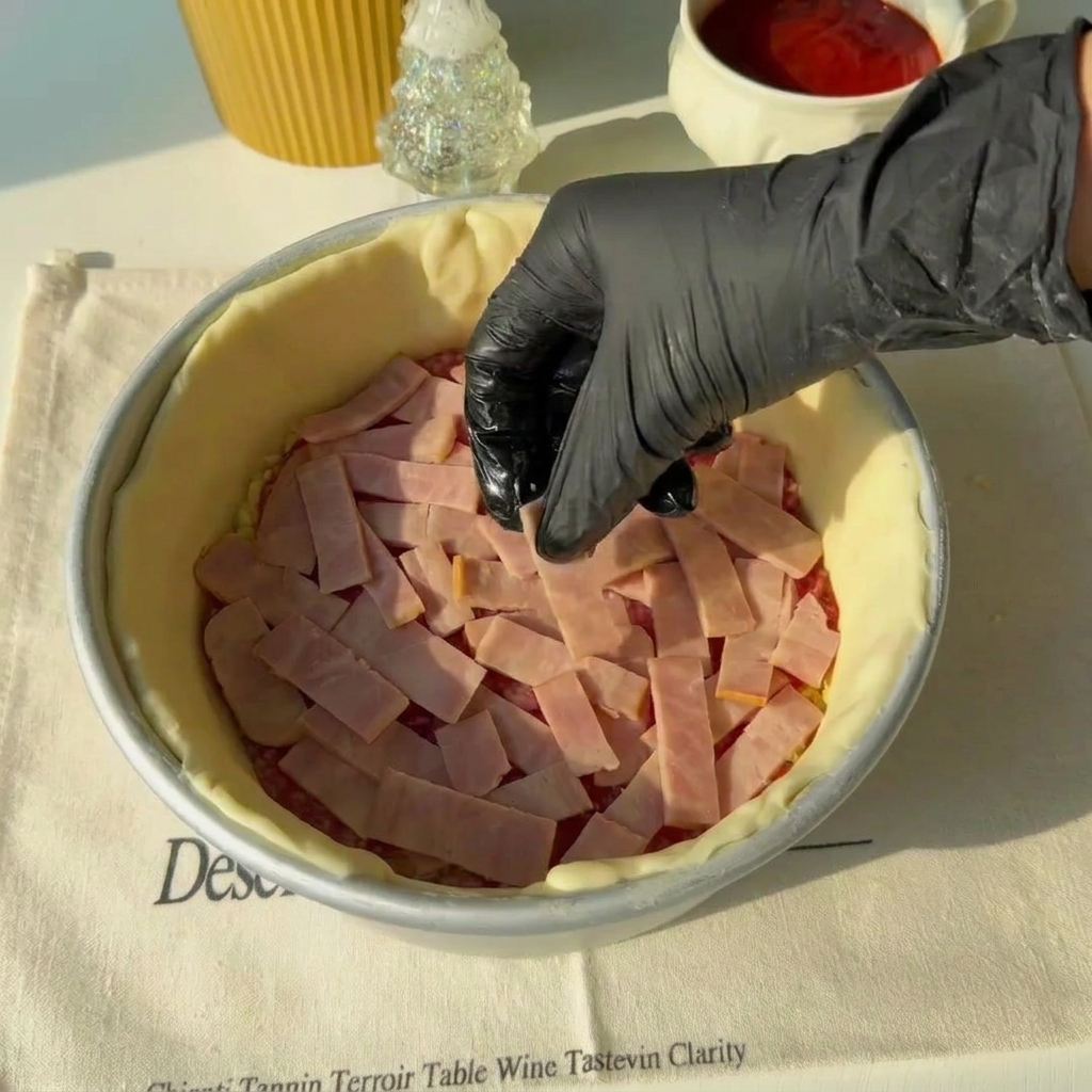 Slices of ham being arranged over the salami layer inside the baking mold.