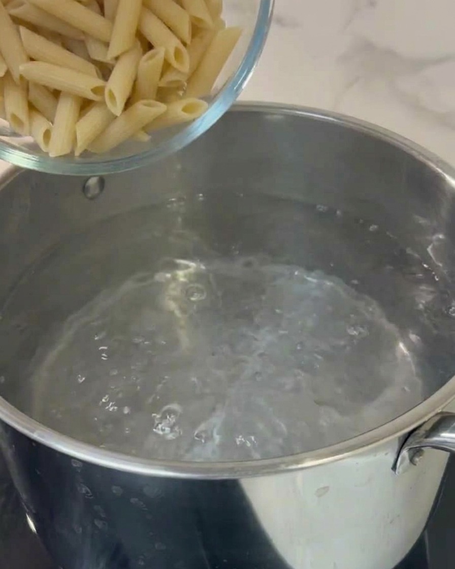 Penne pasta being added to a pot of boiling water.